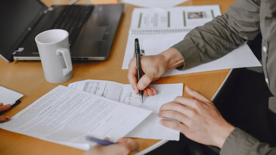 Persona revisando y firmando documentos de cumplimiento sobre una mesa de trabajo
